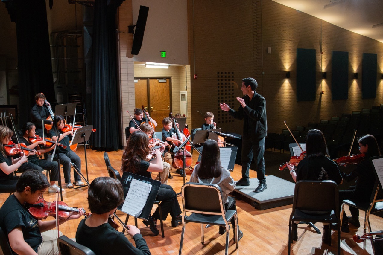 CU Boulder student leads an ensemble of middle school strings musicians in practice before their performance.